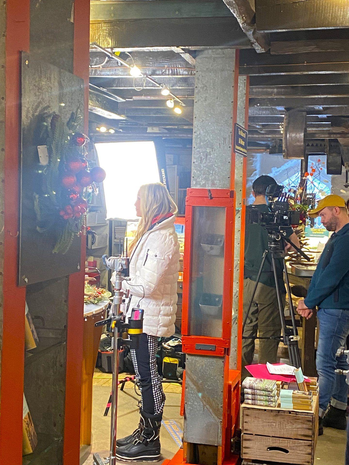 Actress Caprice stands on set during filming in the café while crew members set up cameras. 