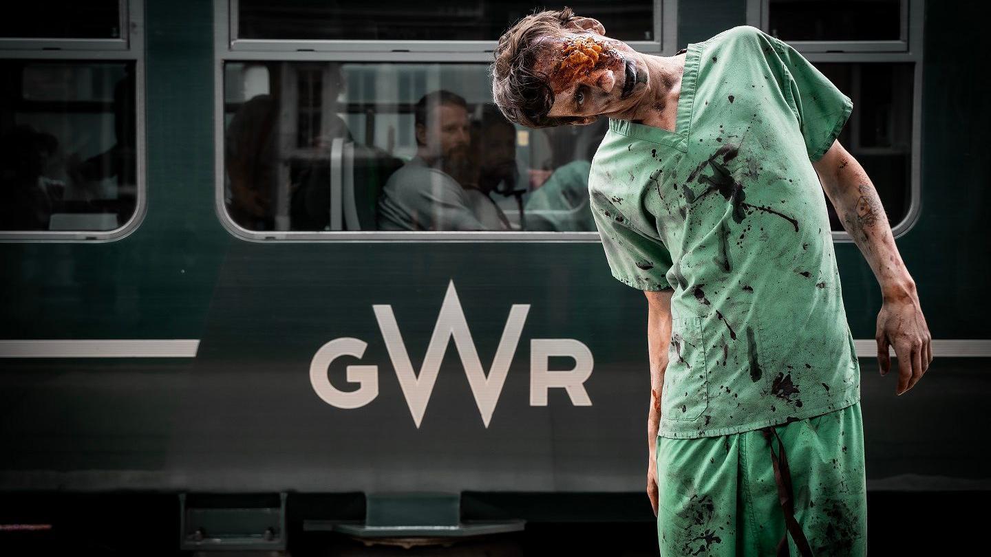 Man dressed as a zombie stands on platform in front of train