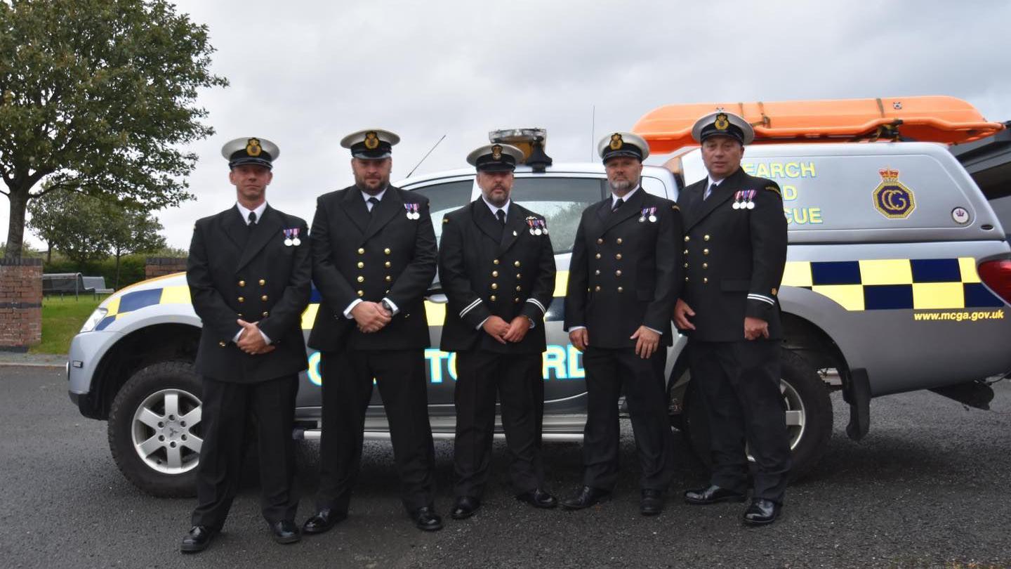 Furness Coastguard members standing together in uniform - wearing their medals - in front of a crew vehicle.