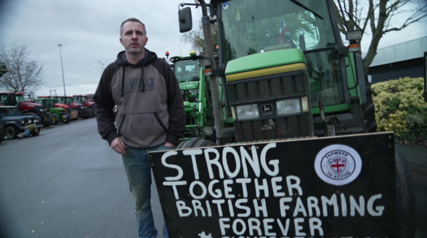 Stephen Carpenter standing next to his green tractor with a sign that says "Strong together British Farming Forever"