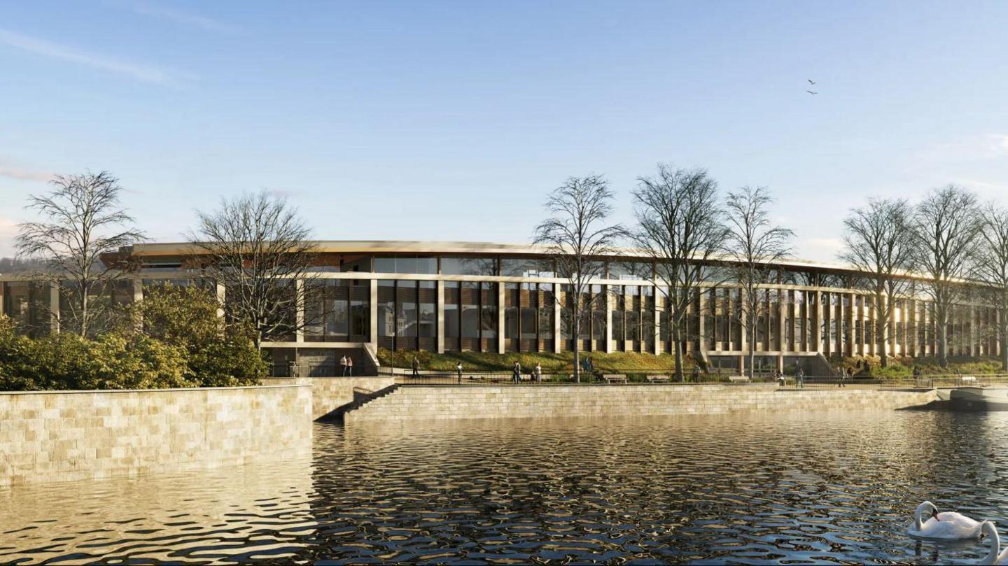 A computer generated image of what the stadium will look like. It is a slightly curved building with large glass windows overlooking the river, where swans are floating. 