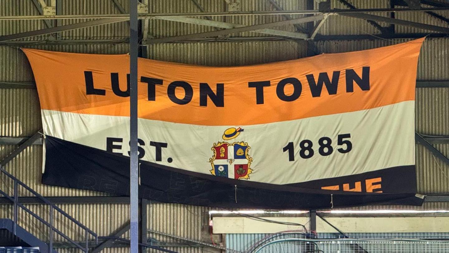 A flag at Luton Town Football club that says "Luton Town Est 1885" with the bottom of the flag pinned up.