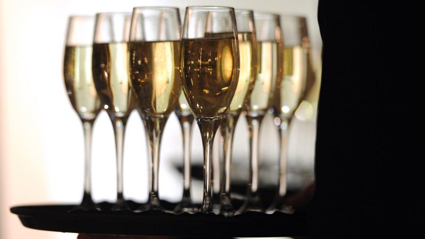 A tray of champagne flutes being carried by someone in silhouette. 