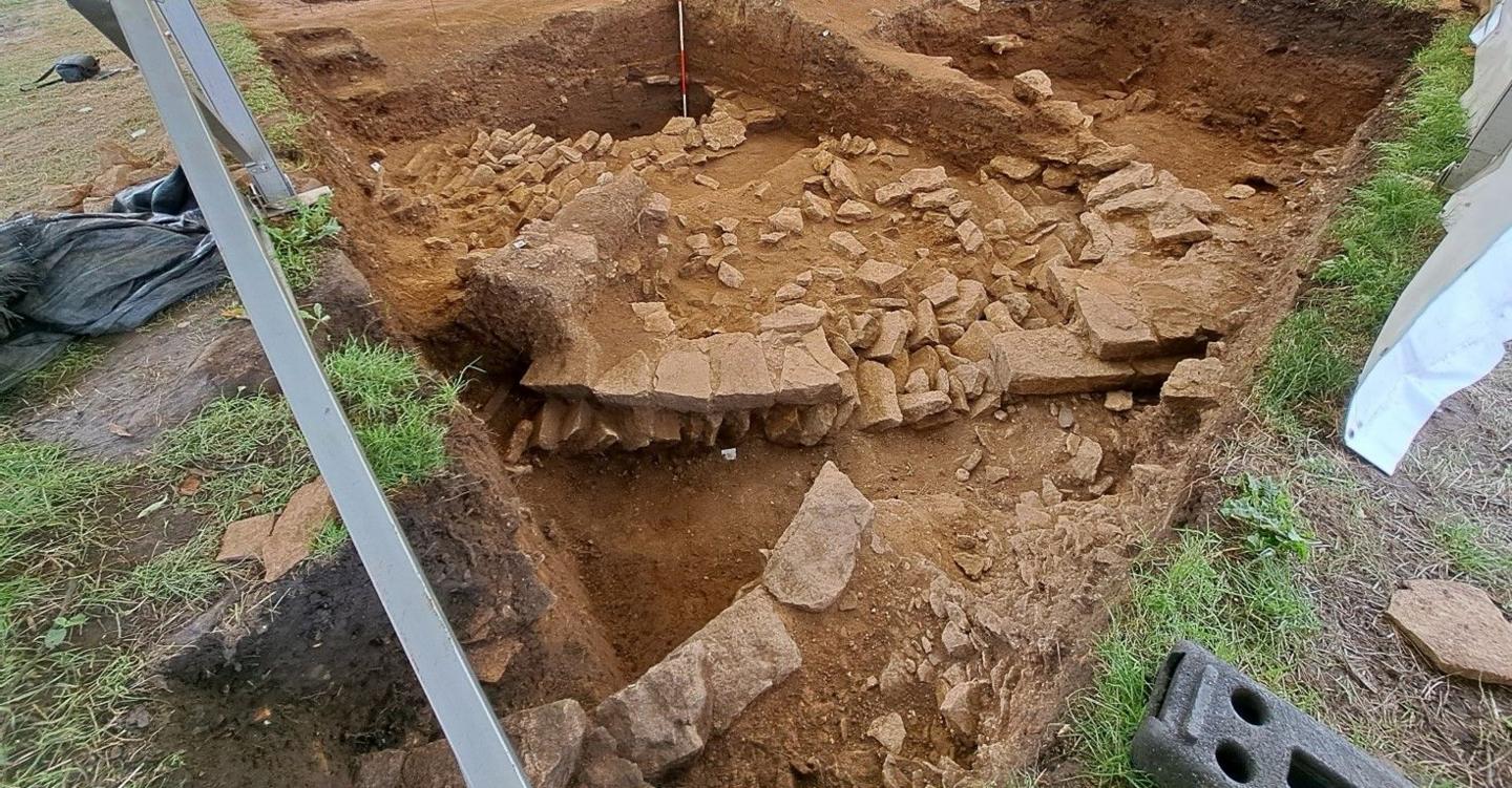 An excavation trench with the stone remnants of the walls of Roman fortifications, which have been uncovered in the light brown earth