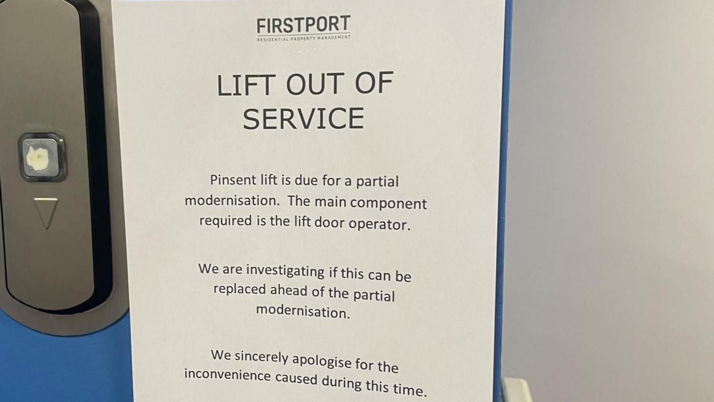 An 'out of order' sign placed next to a lift. It say "Lift out of service. Pinsent lift is due for partial modernisation. The main component required is the lift door operator. We are investigating if this can be replaced ahead of the partial modernisation. We sincerely apologise for the inconvenience caused during this time."