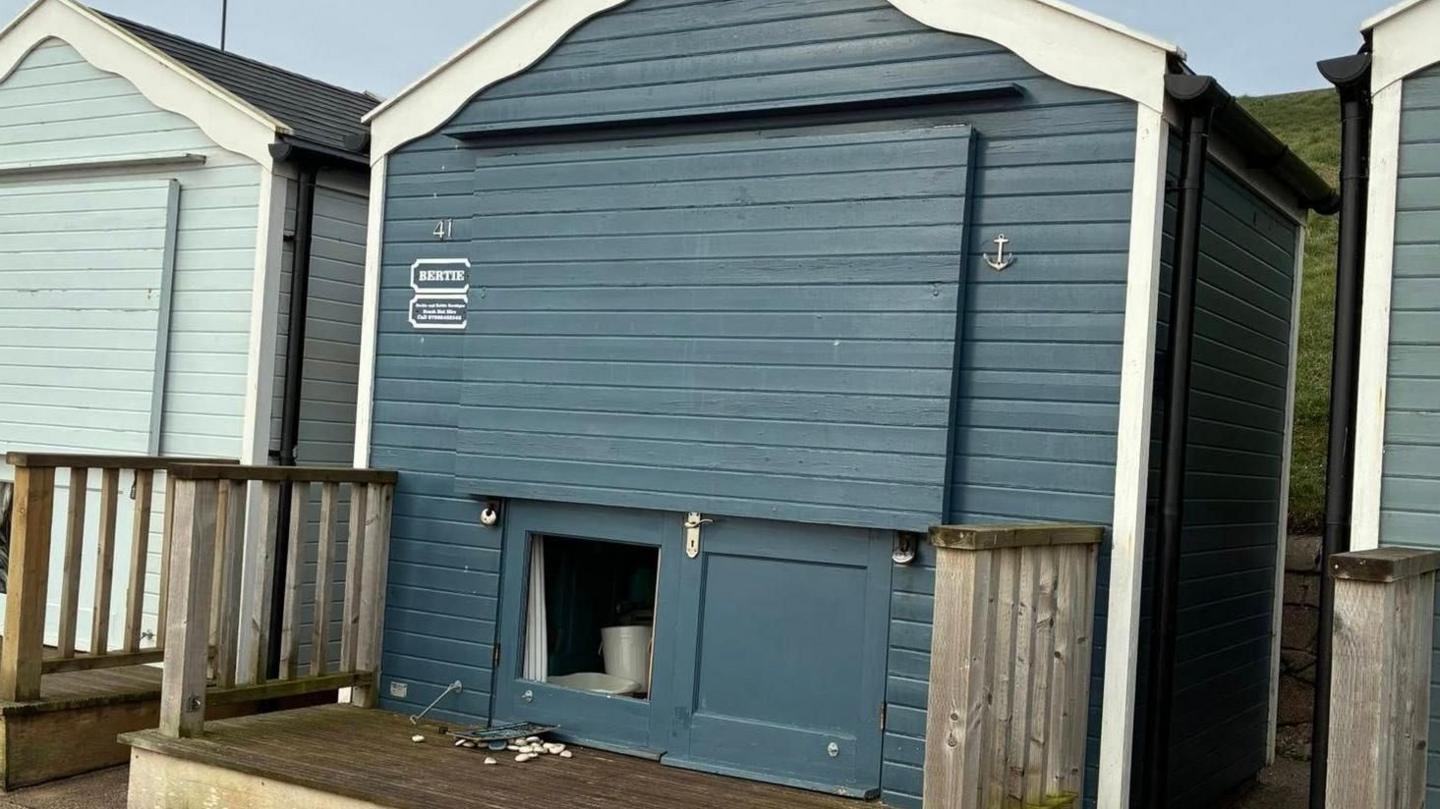 A close up of a navy beach hut with its lower panel removed, which was the way the intruder gained access. The hut has decking to its front. 