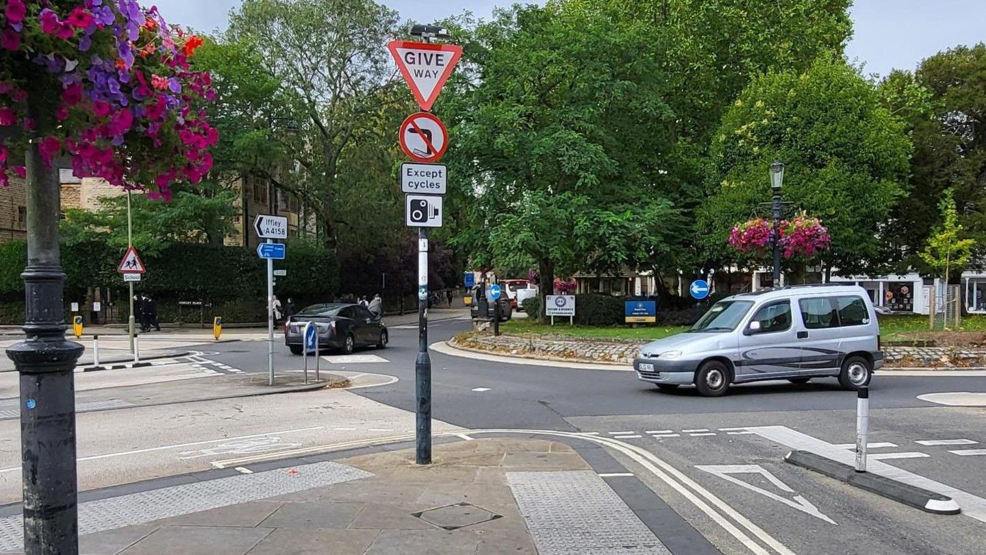 The Plain Roundabout in Oxford. In the foreground is the extremely sharp left turn from the Cowley Road to the Iffley Road. On the corner is a lamppost with a sign saying no left turns and an image of a camera.