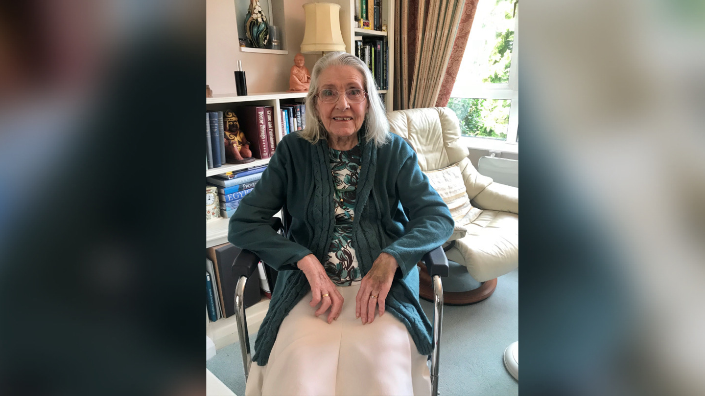 Irene Wright in a wheelchair. She has grey hair down to her shoulders and glasses, in a green cardigan, a flowery top and a beige skirt