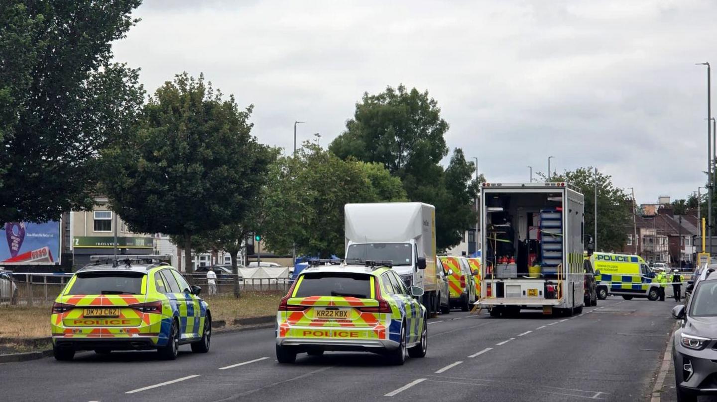 A number of police vehicles close off dual carriageway in Merseyside. The road has trees lined down the middle