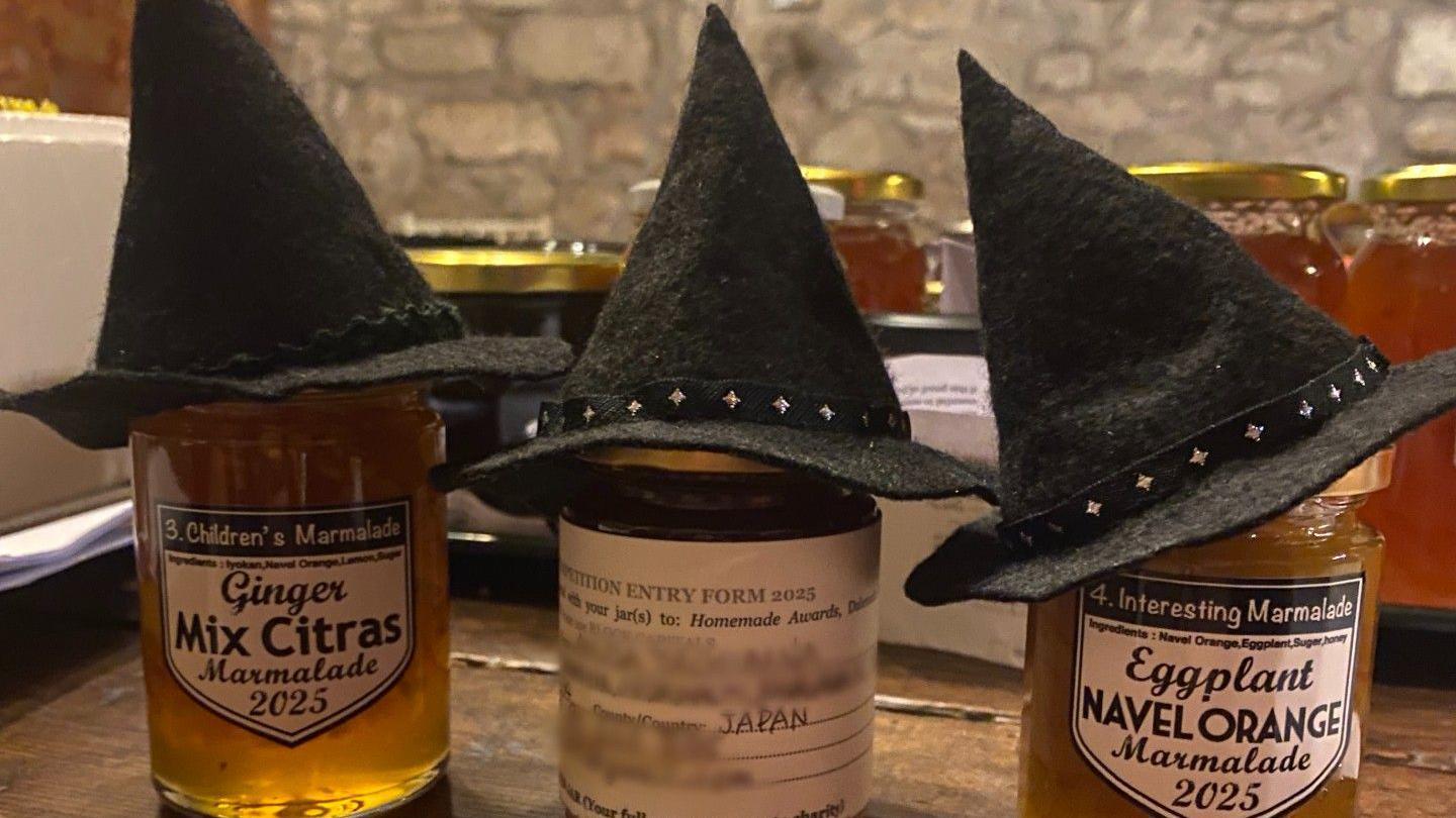 Three jars of marmalade wearing black witches' hats.