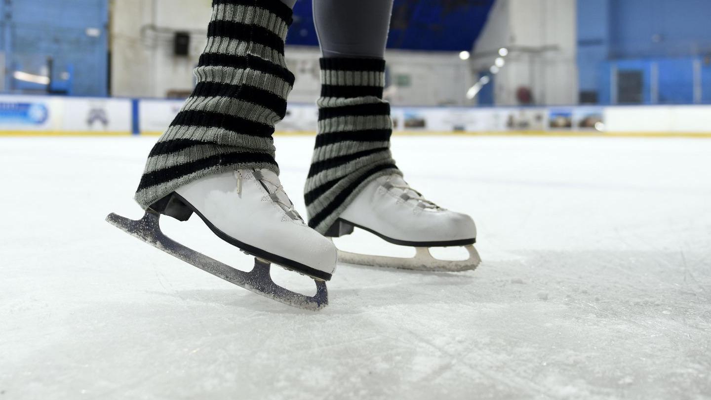 A close up shot of a pair of ice skates with black and grey striped socks over the white boots 