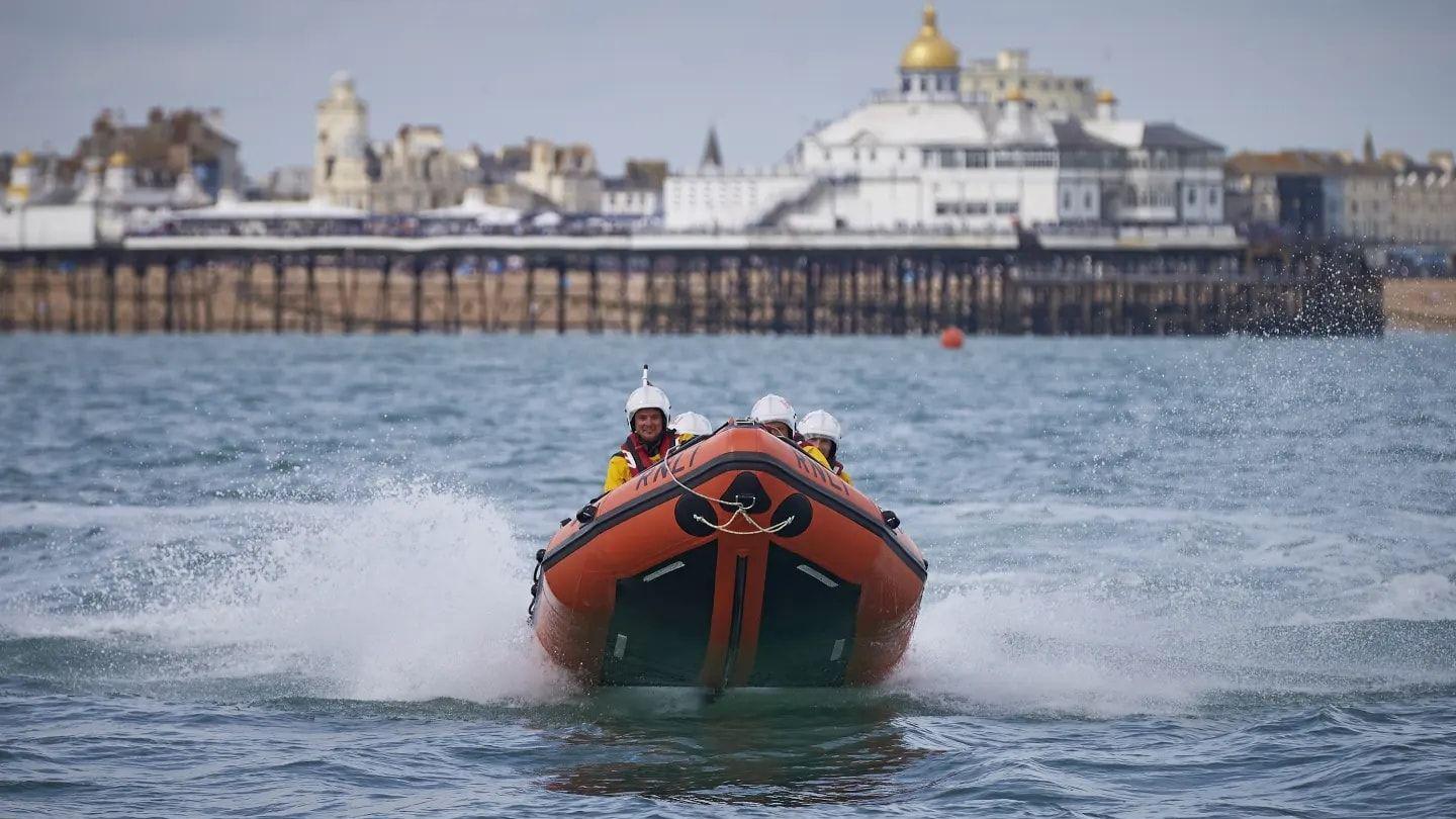 An orange lifeboat dinghy with people in it on the water. A pier with a gold roof is in the background.