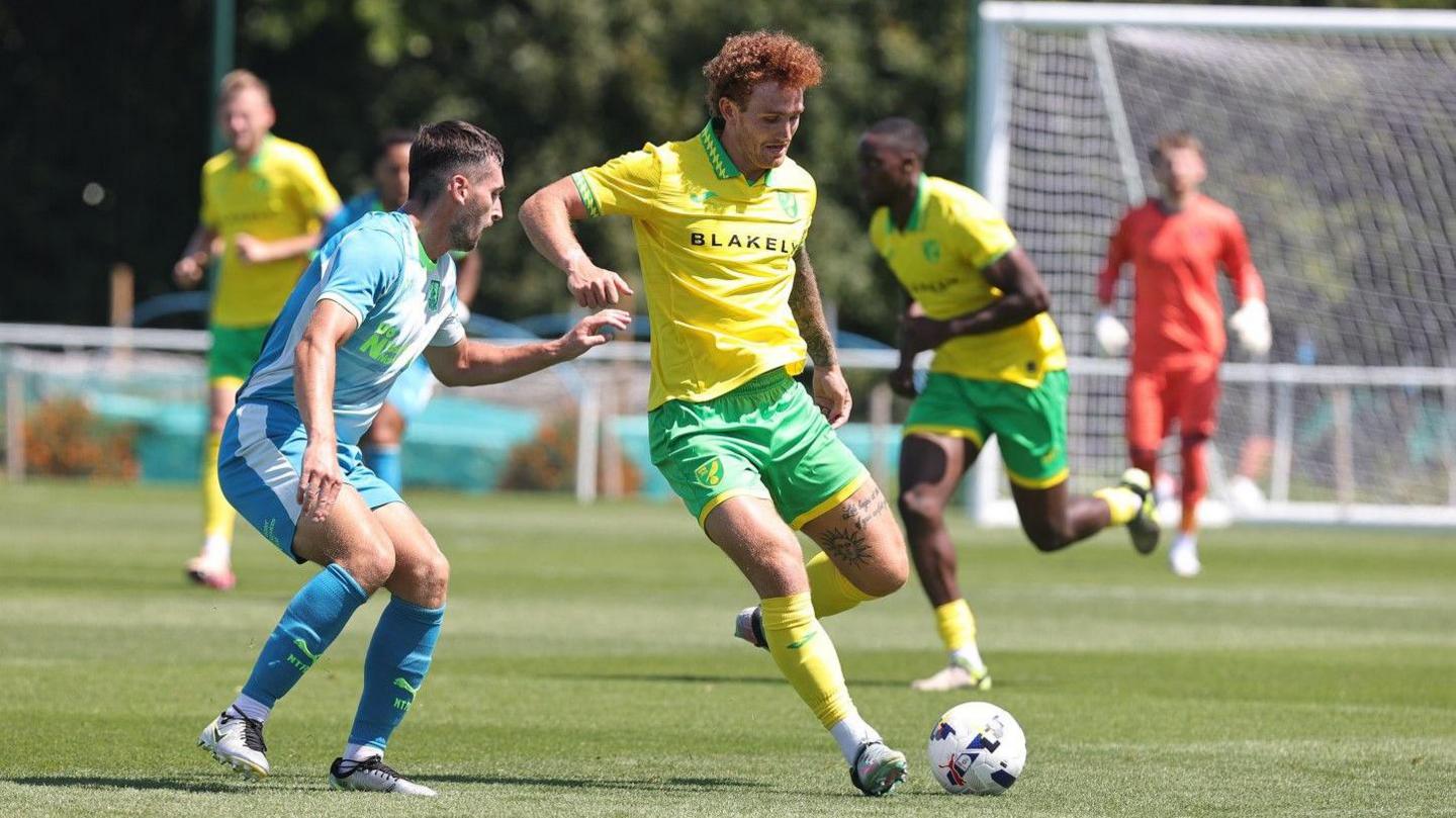 Two opposing football players battle for the ball in a match
