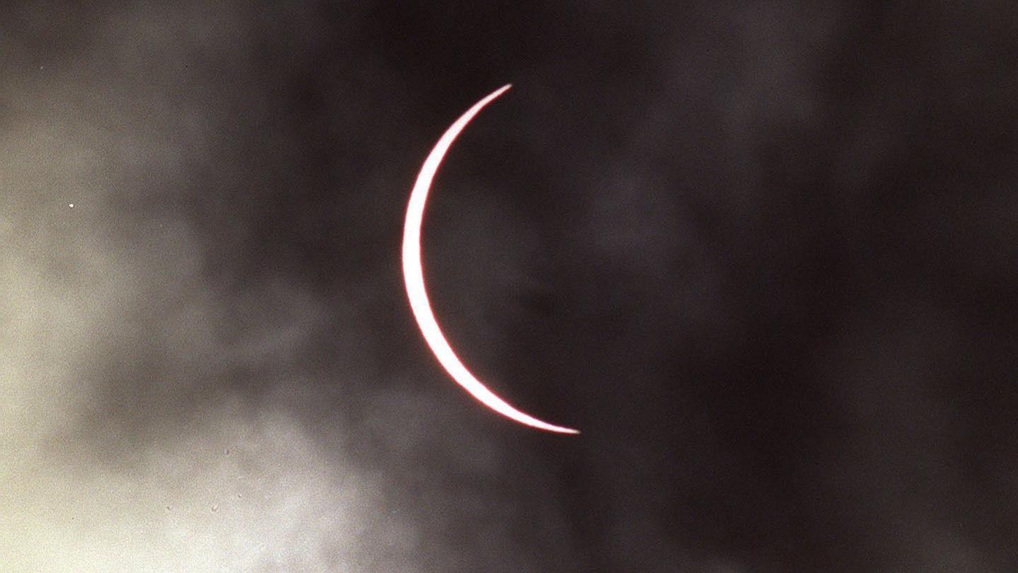 The moon has moved across the sun leaving a thin band of the sun visible which has taken on a pink hue. The sky is cloudy.