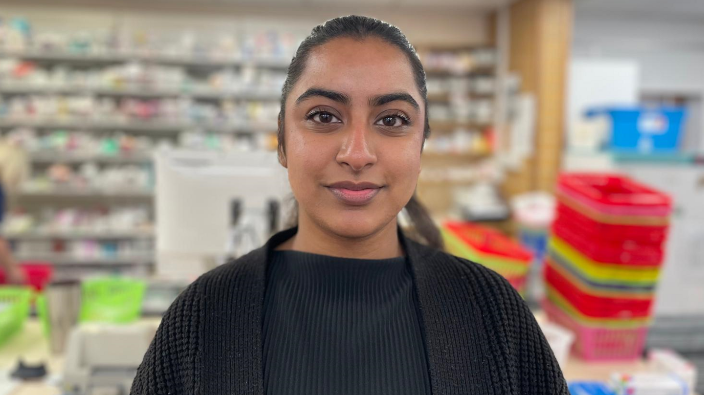 Trainee pharmacist Roshni Landa stands in front of drug supplies and trays at a pharmacy in Leeds