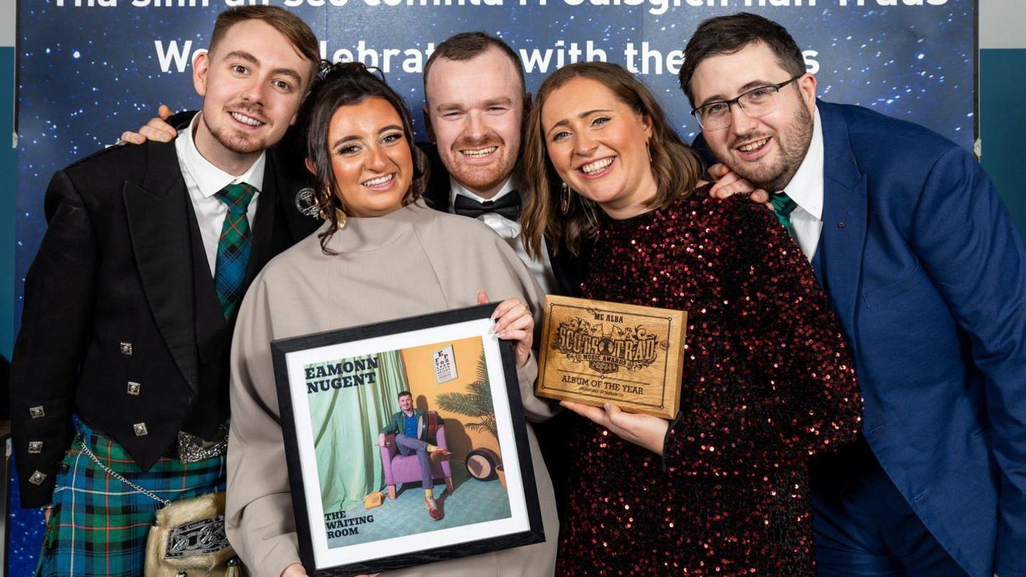 Eamonn's friends and family are standing together holding his award and a framed photograph of his album cover.