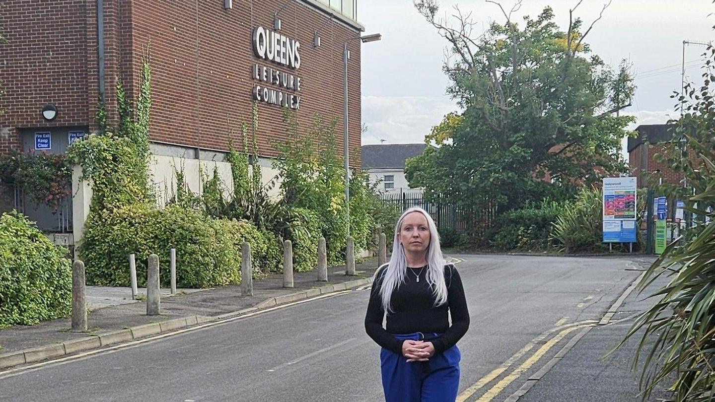 Lauren Kendall wears a black long-sleeve top and blue jeans. She is standing on a road 