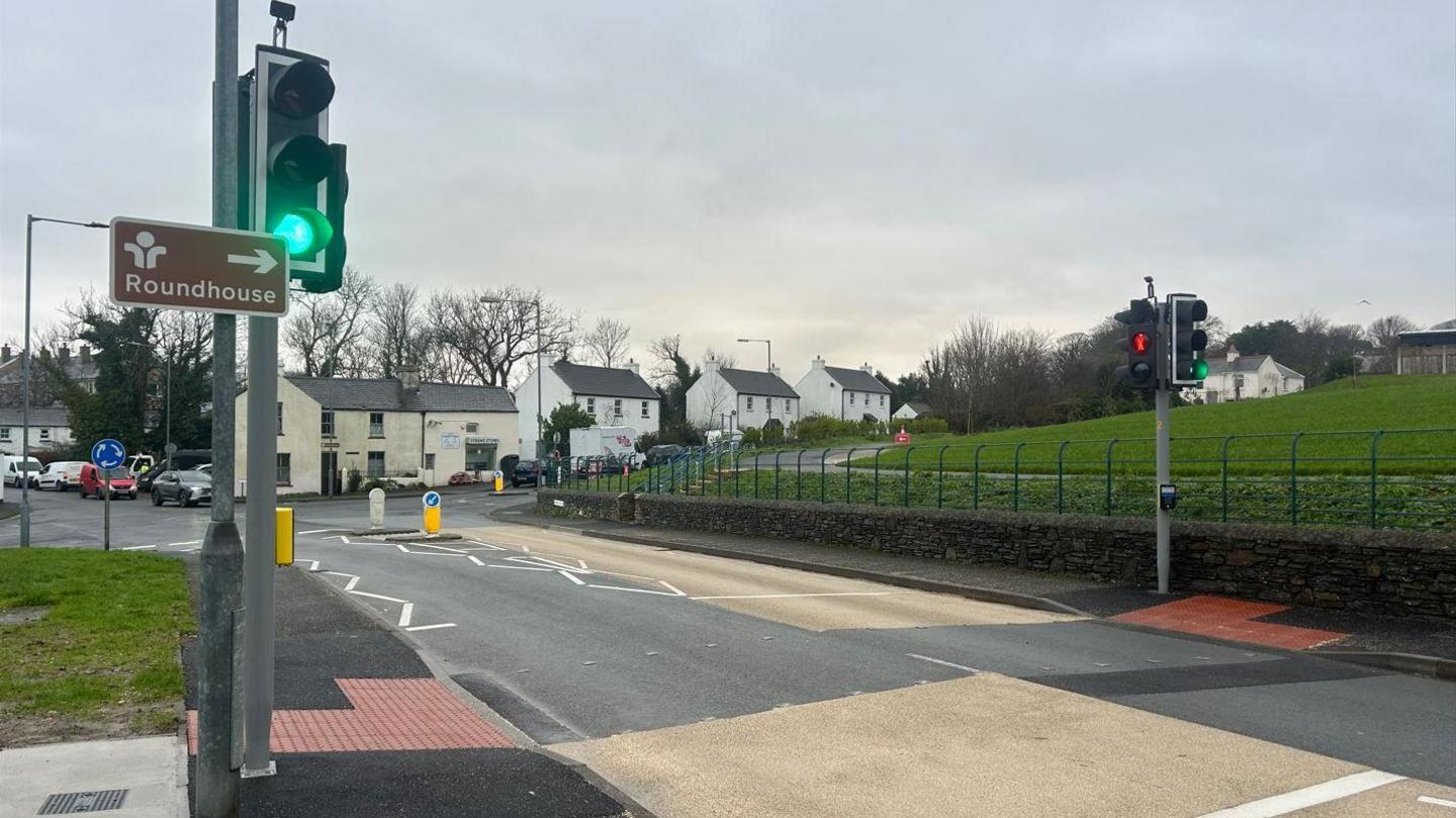 The puffin crossing, which has traffic lights that are on green, and a brown sign that reads Roundhouse with an arrow above it attached to the pole.