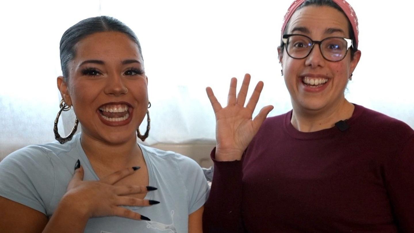 Chanice and Sara smile while sat on the sofa