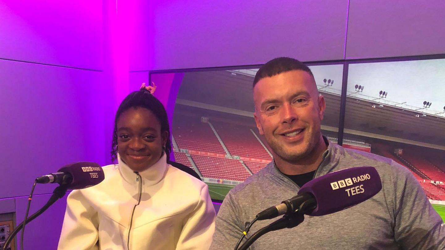 Celine Obinna-Alo (left) sitting behind a BBC Radio Tees purple microphone next to coach Richard Kilty