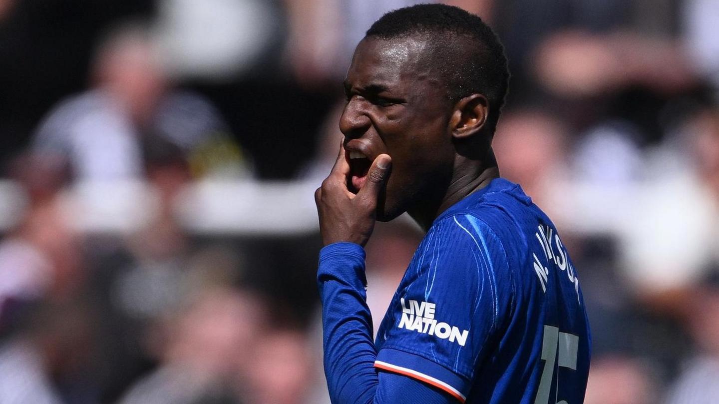 Nicolas Jackson, wearing a blue Chelsea shirt, holds his chin and grimaces