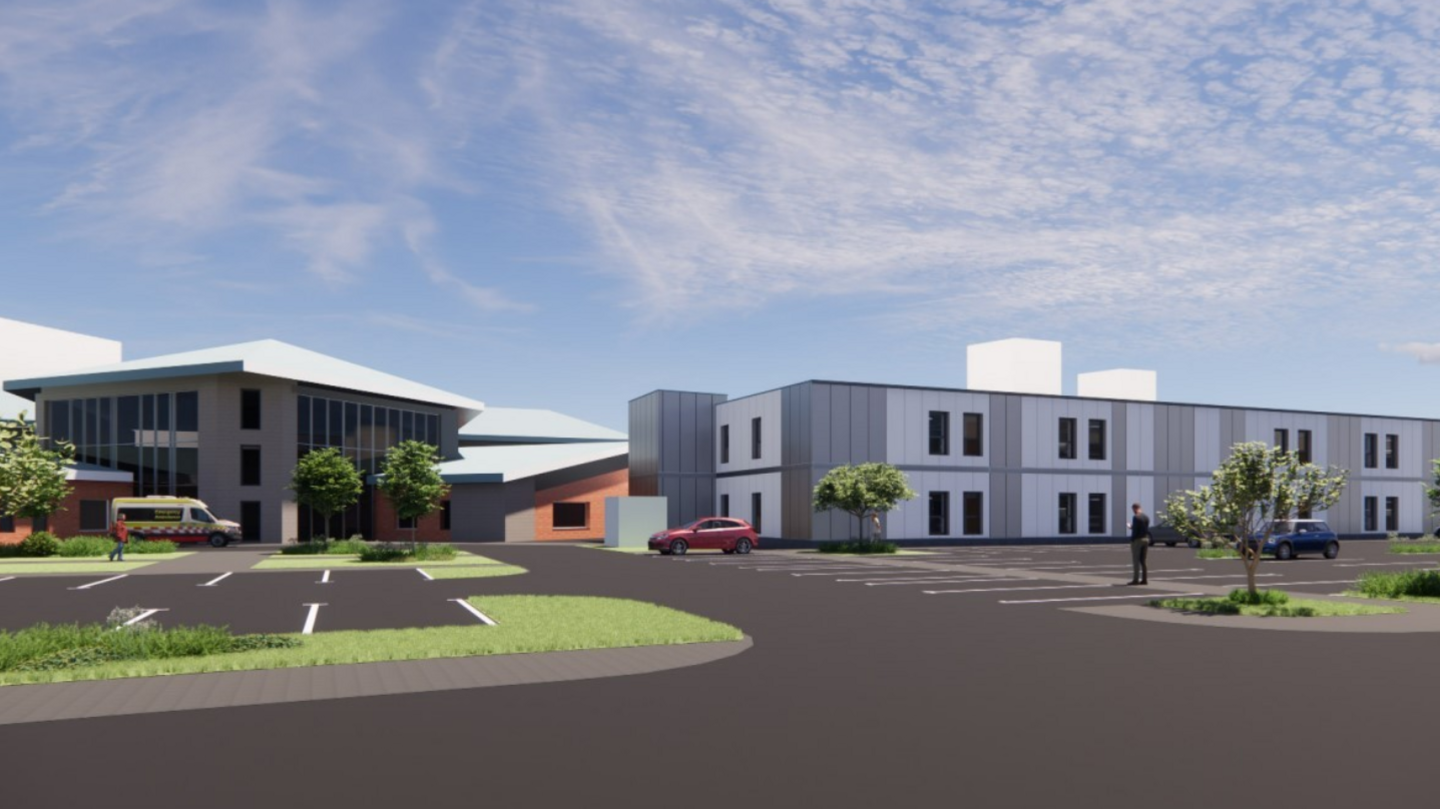 A computer generated image of the proposed two-storey hospital. It is is a white building and there is a car park with a red car, blue car and ambulance.