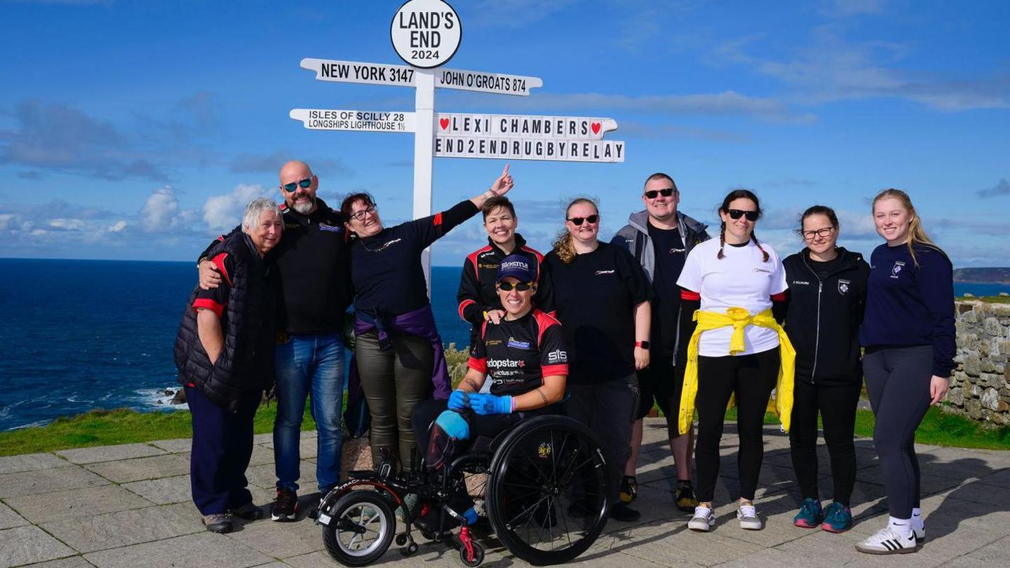 Lexi and her support team standing next to the Land's End sign-post when she finished the challenge