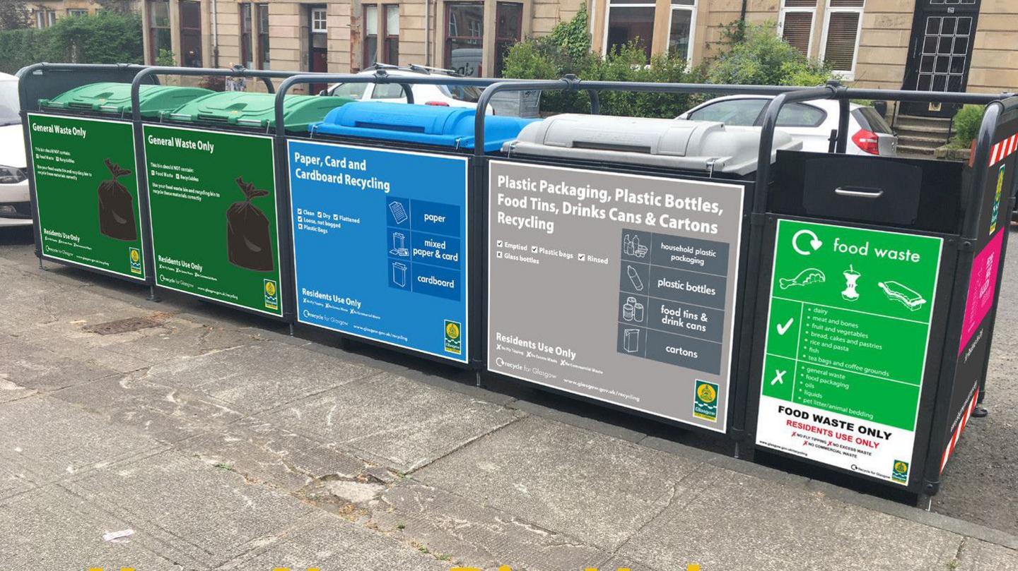 A row of large bins, placed on the street beside the pavement. Each one has instructions about what to put in it. 