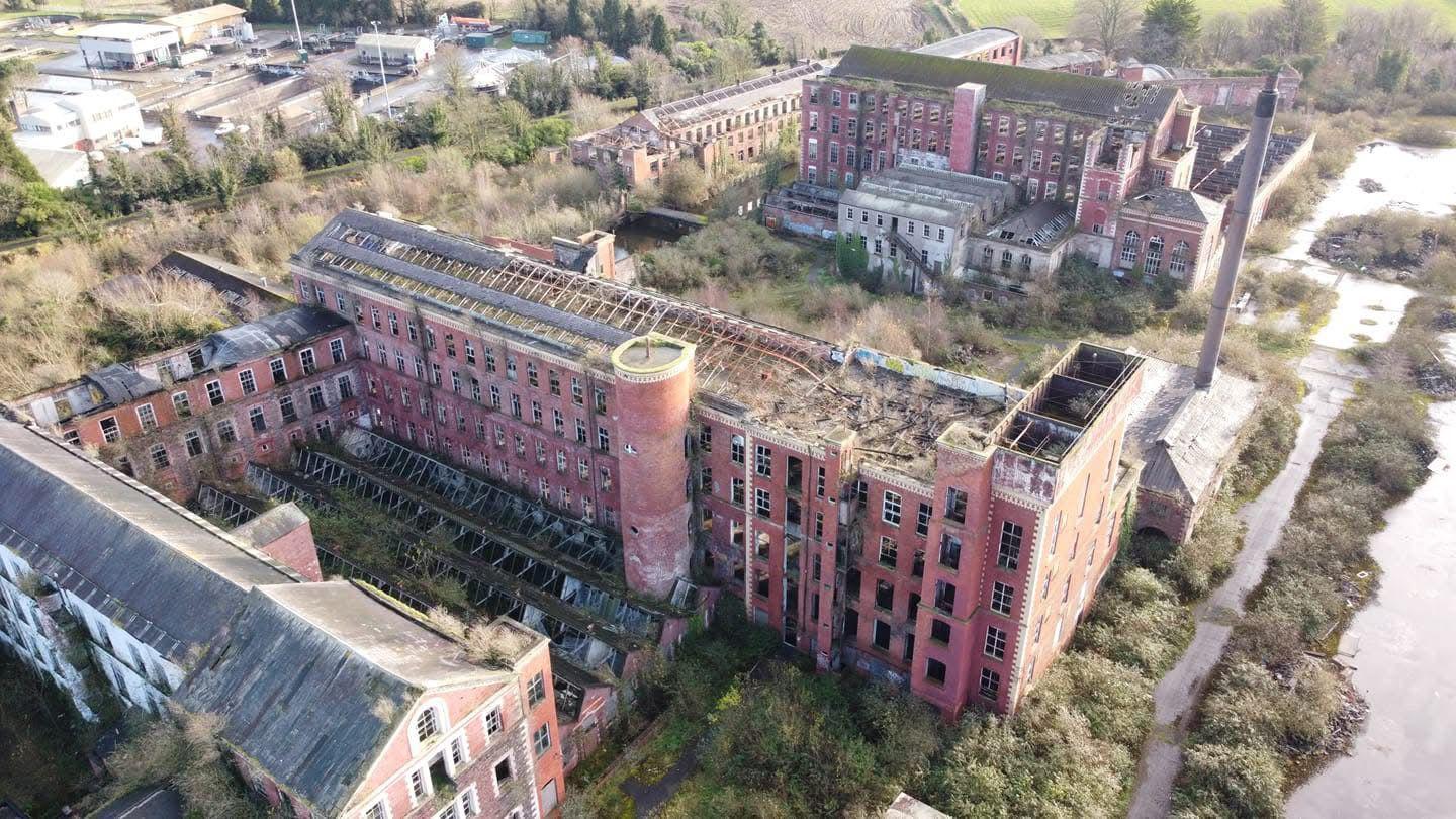 An aerial view of Hilden Mill. It shows extensive fire damage along the roofs of each building and overgrown shrubbery.