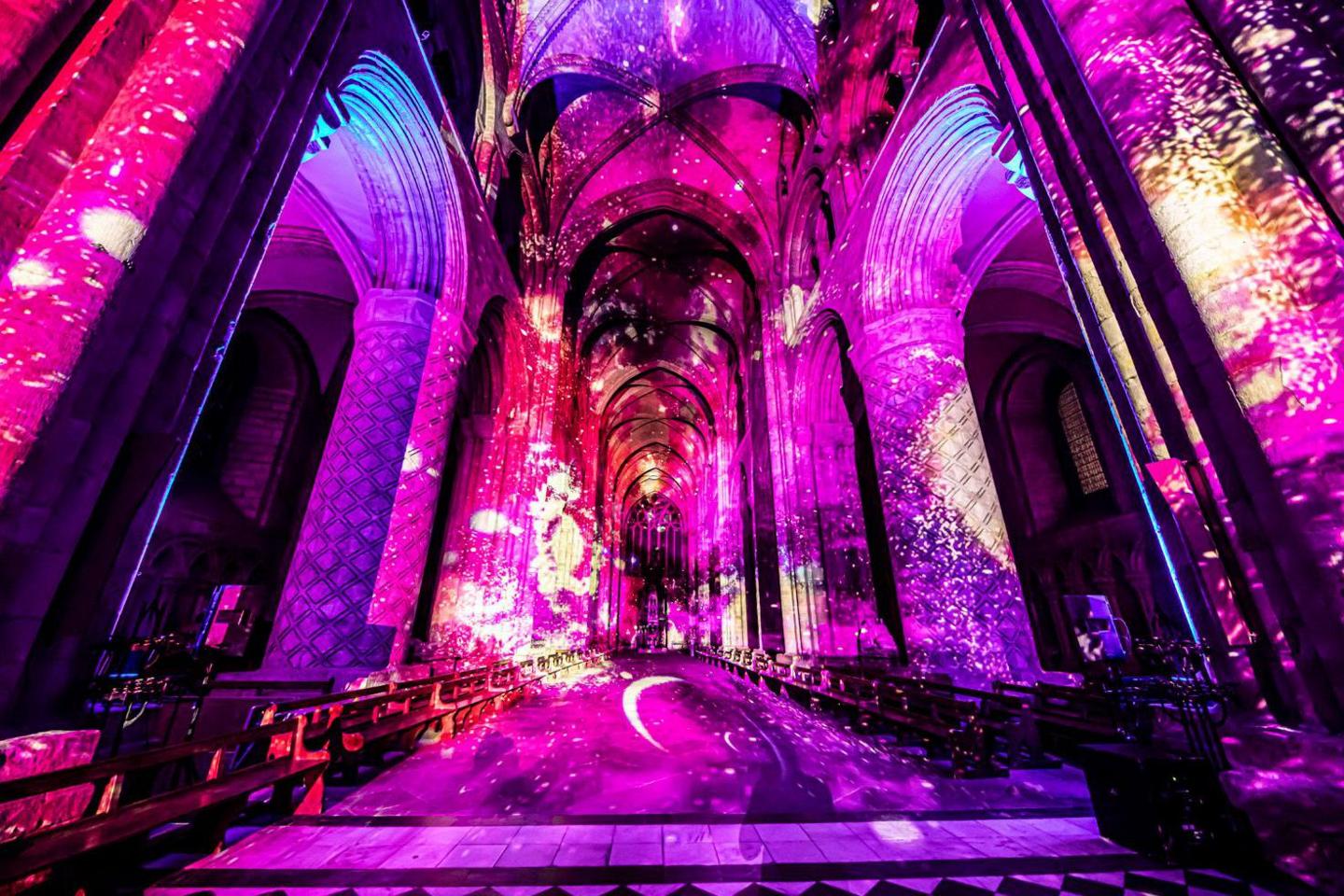 Pink, purple and red projections on the cathedral. A yellow moon crescent is projected on the floor. 