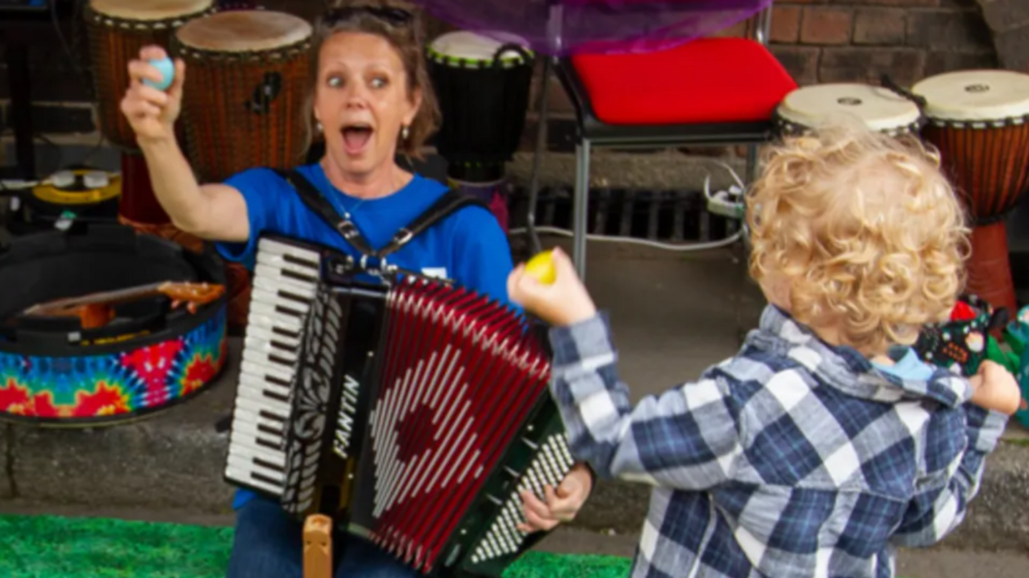 A woman with an accordion entertaining a child with blonde hair