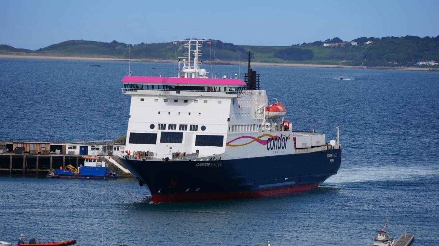 A Condor ferry arriving at a harbour in Guernsey. The ferry is predominately white with a dark blue base, with some pink trimming. 