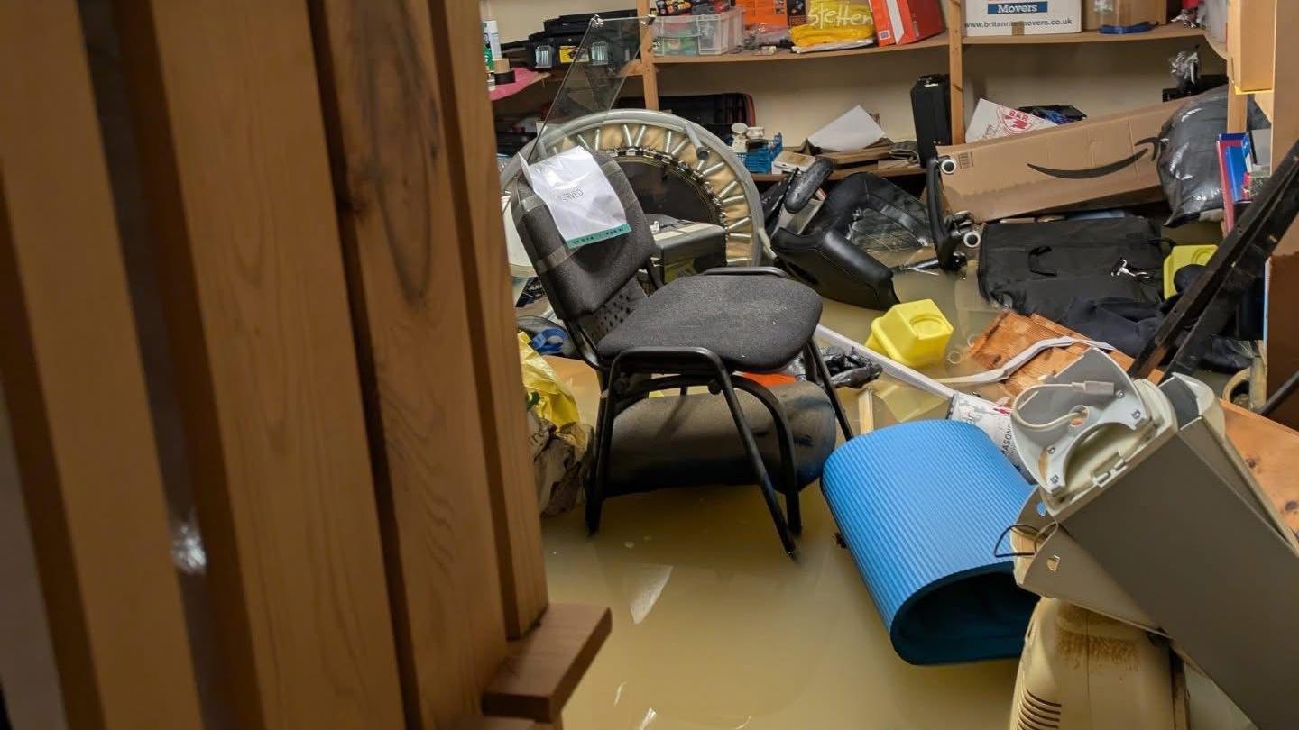 A basement with various items in it which has been flooded with brown, muddy water. 