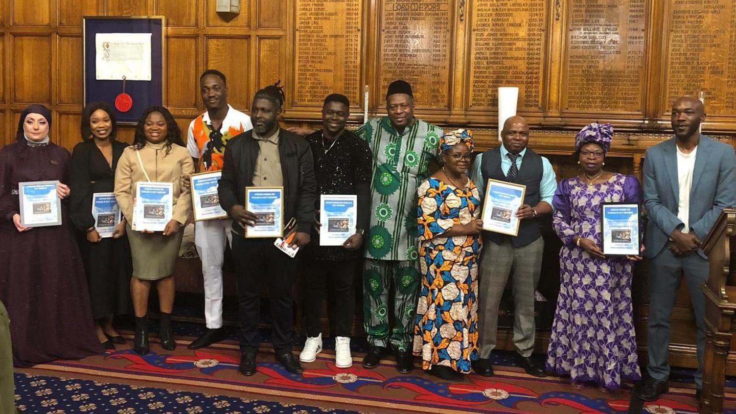 A group of people in traditional African clothes pose holding award certificates