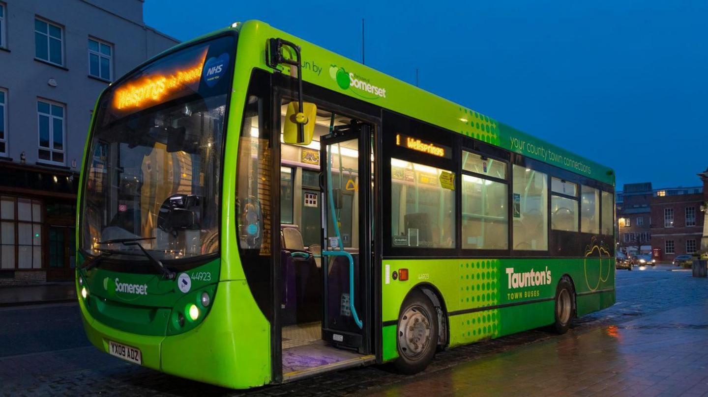 A green bus in Taunton driving at night