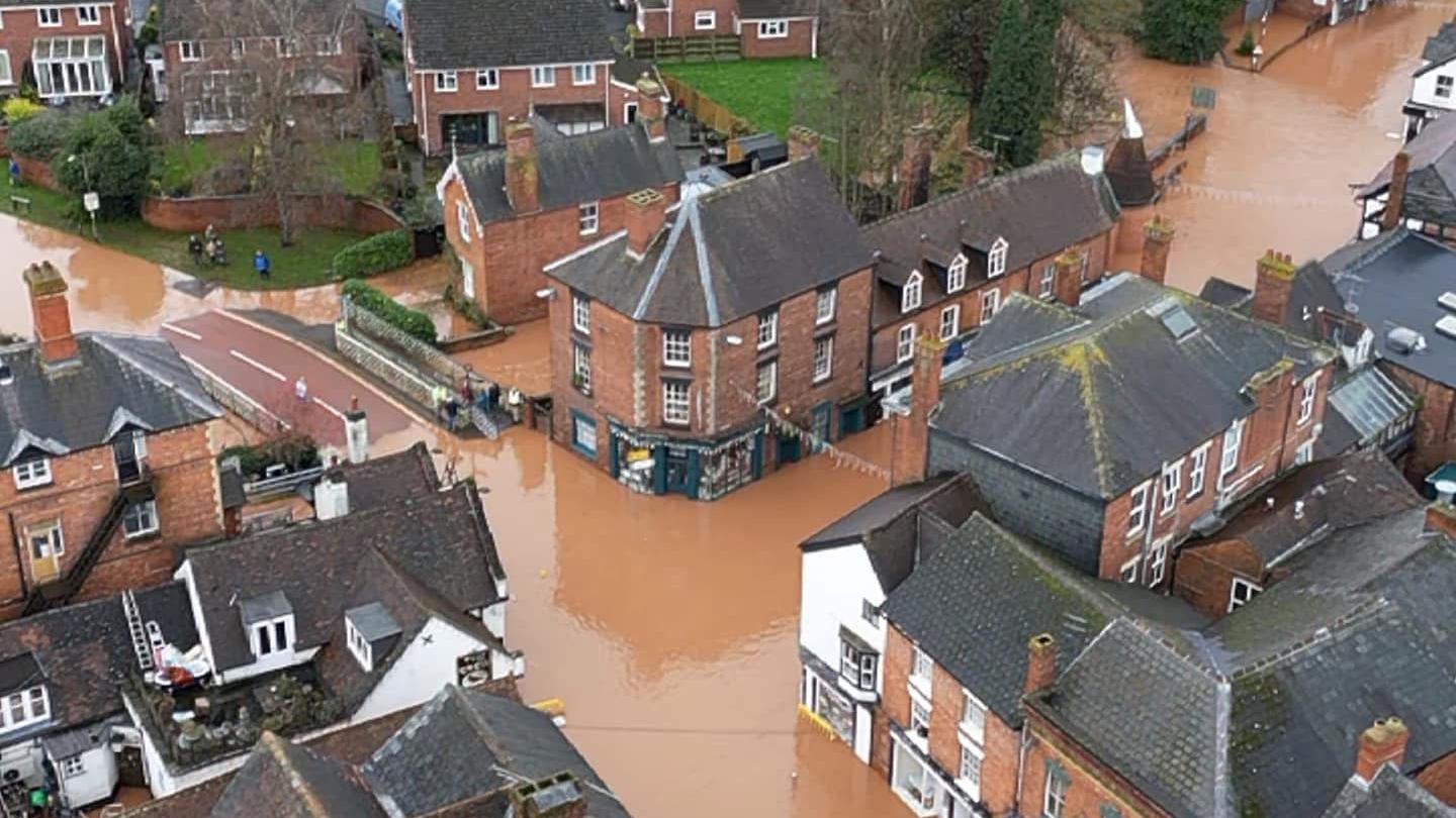 An aerial view above Tenbury - showing rows of houses surrounded by flood water which is covering the pavements and roads.