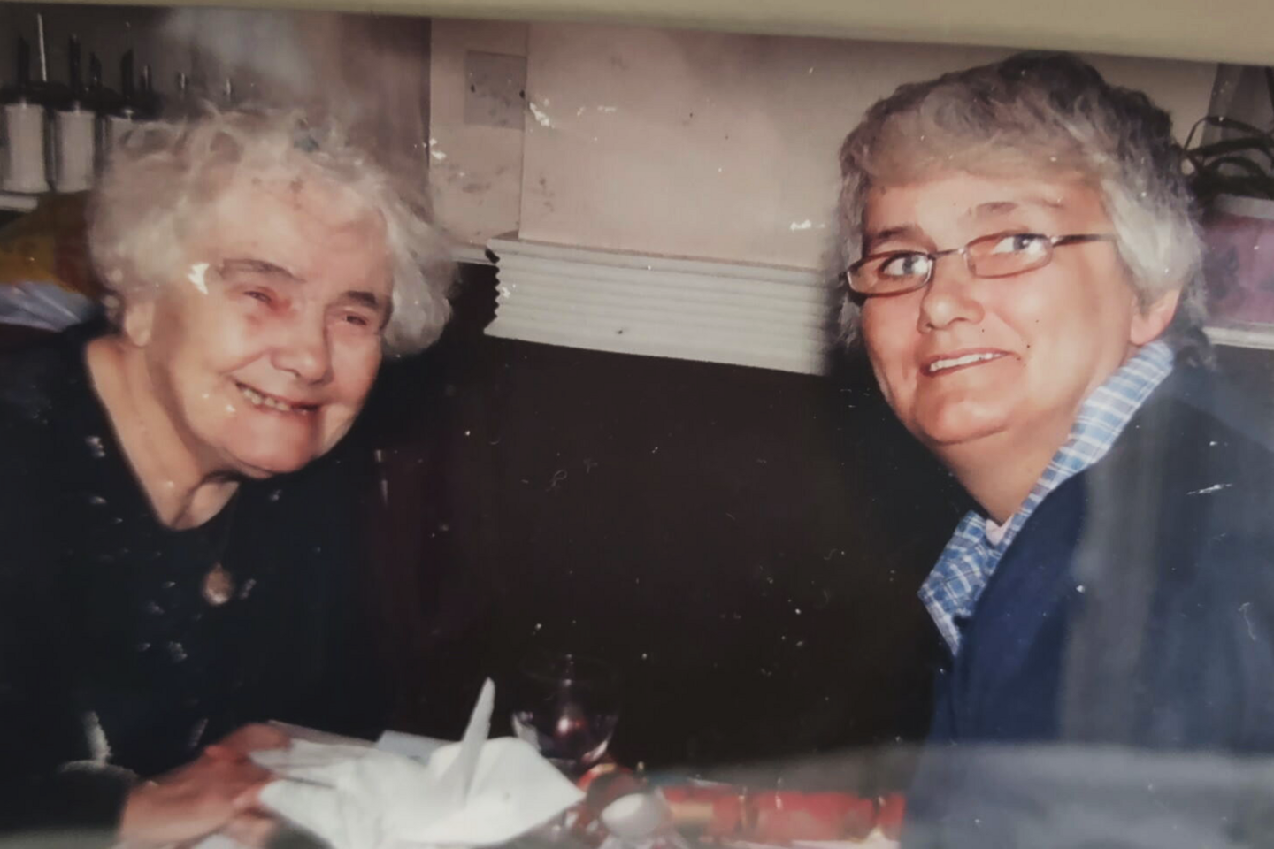 A grainy old photo of Patricia Allison, an elderly white-haired woman, sitting across a table from her daughter Anne, a younger grey-haired woman in glasses.