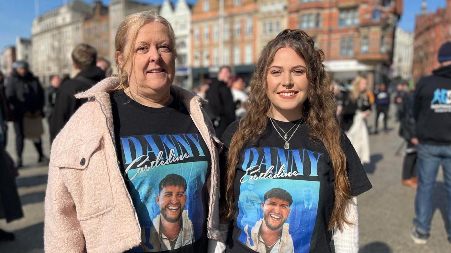 Two women - the mother and daughter of a man who died when he was stabbed - stood next to each other outside wearing matching black t-shirts. On the t-shirt is a photo of their loved one who died - Danny. 