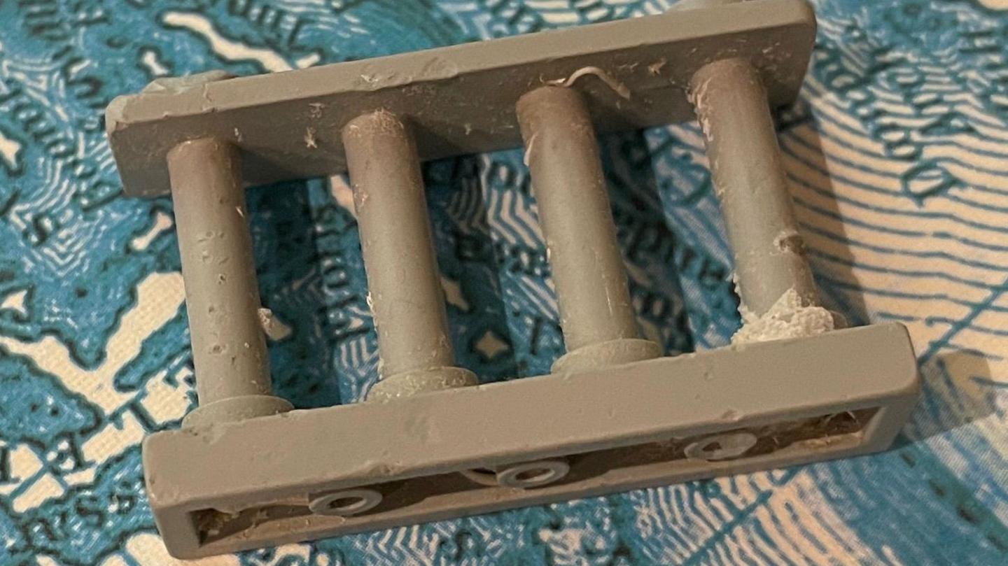 The grey panel has four rungs inside a frame and looks a bit like a chunky ladder. It is lying on a blue and white map showing the sea.