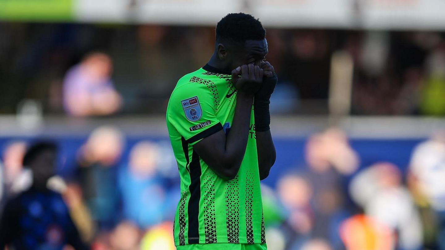 Ebou Adams covers his face after Pompey's defeat at QPR