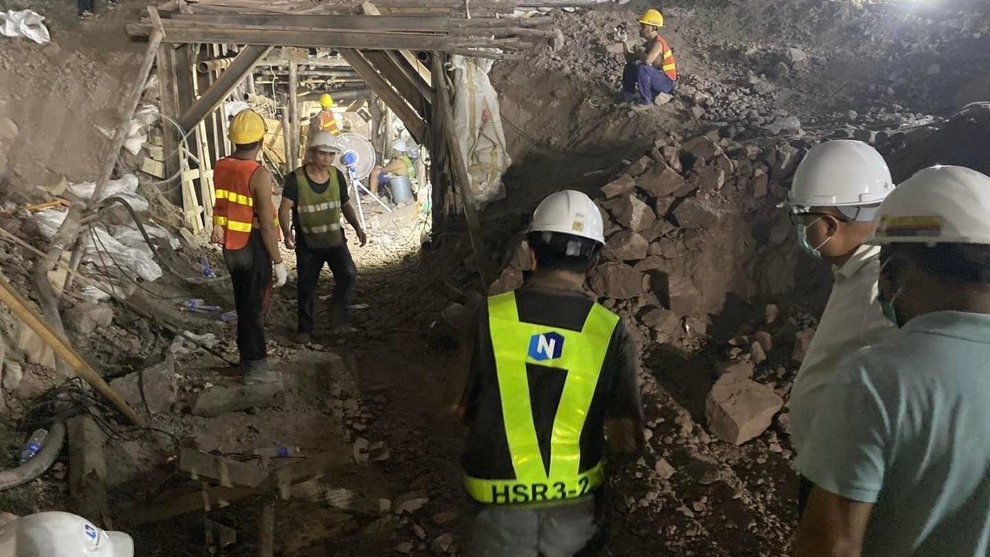 Rescue workers, wearing white helmets and florescent jackets, dig through a tunnel looking for the trapped workers