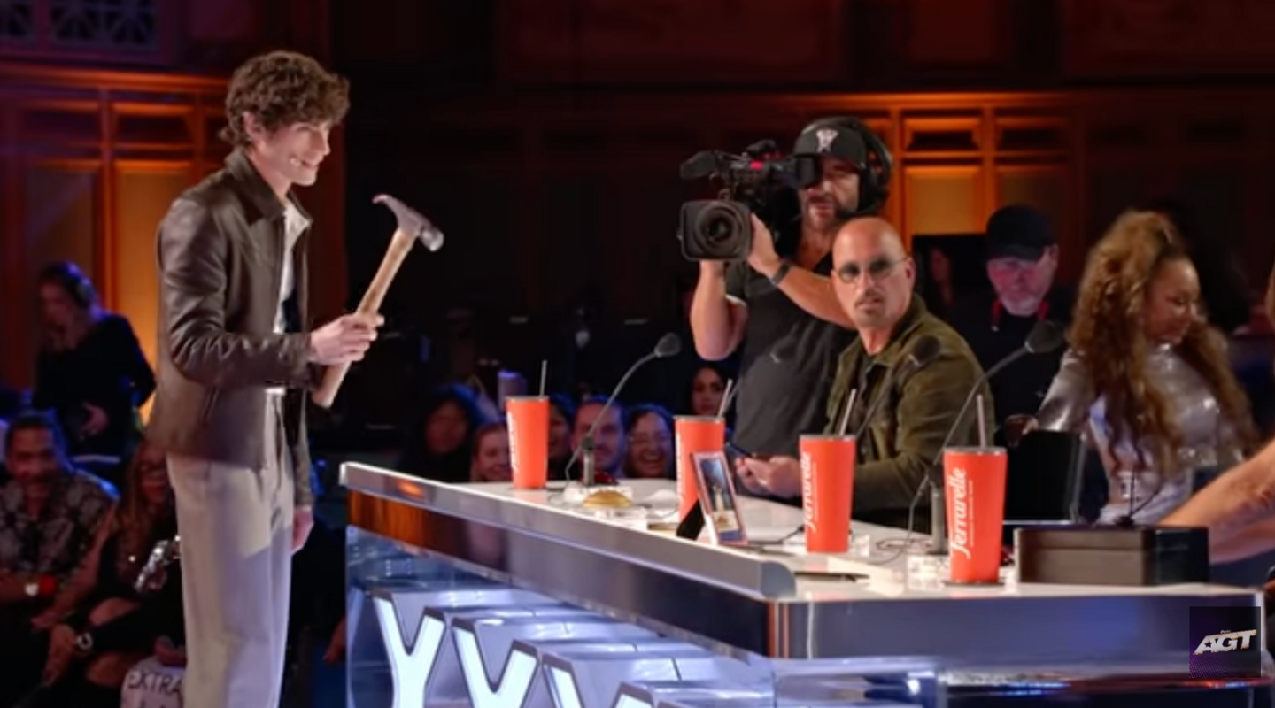 Joel seen holding a hammer in front of the judges table 