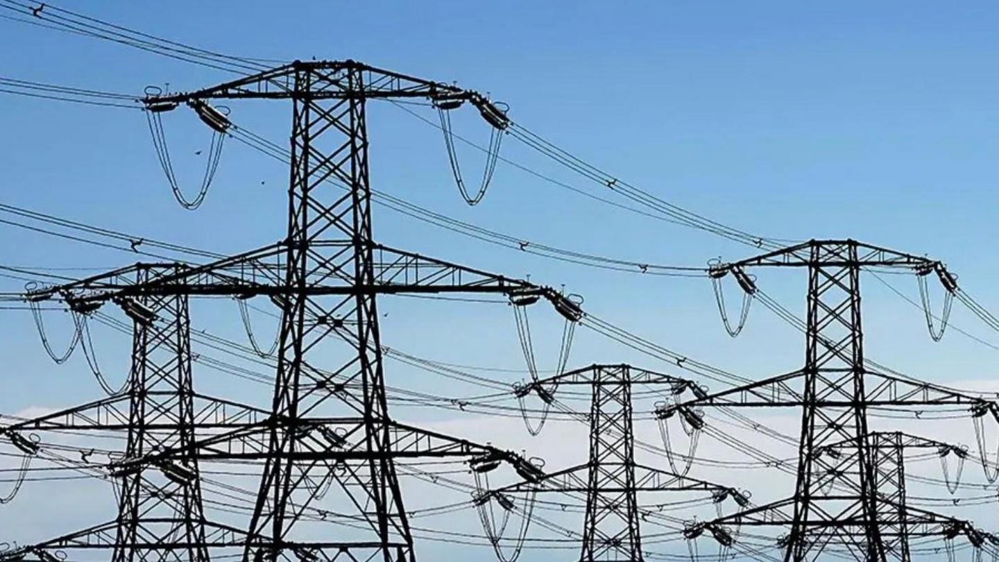 A number of pylons and cables are seen against a backdrop of blue sky.