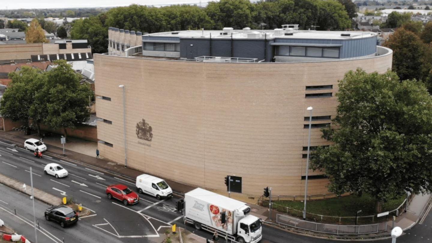 An aerial shot of Cambridge Crown Court on a dreary day, with its curved walls and a large tree the focus of the image. Traffic queues parallel to the court.