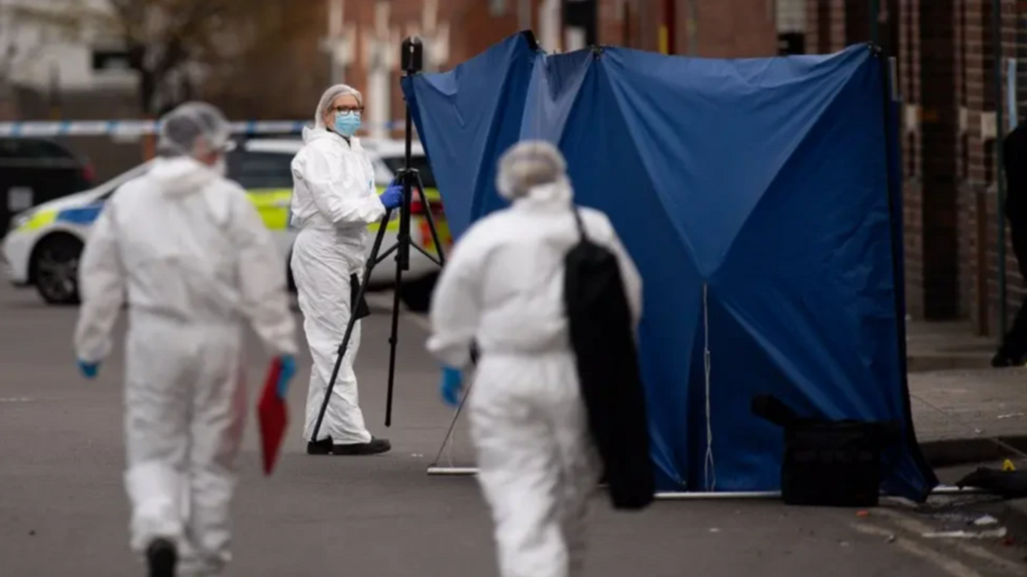 A forensic crime scene showing officers in white PPE and walking towards a blue police tent.