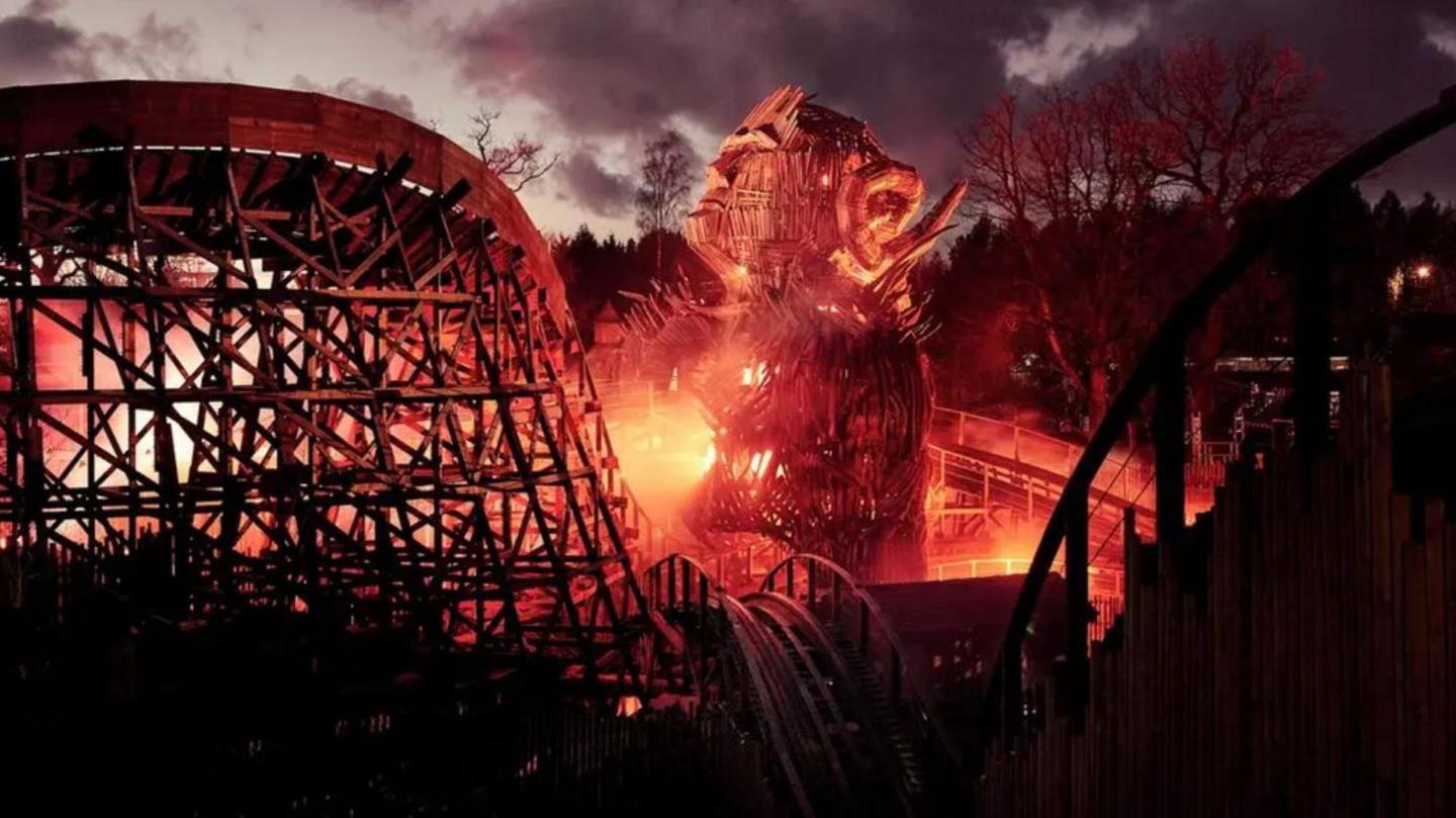 A wooden rollercoaster at night with flames lighting up the centre of it