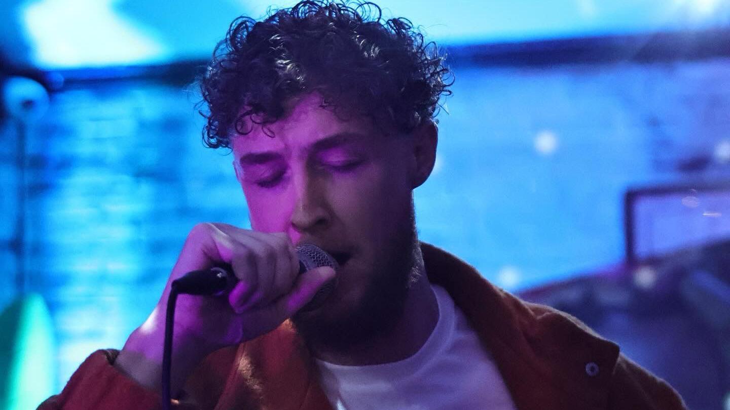 Ryan Finan with brown hair has his eyes half closed as he sings into a microphone against blue lighting.