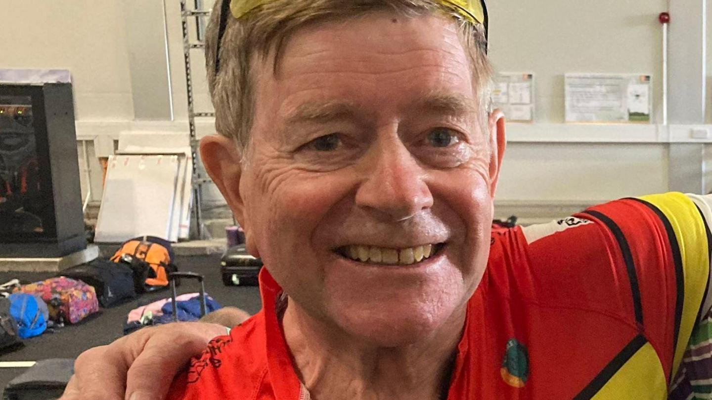 A man in a red cycling top smiling at the camera.