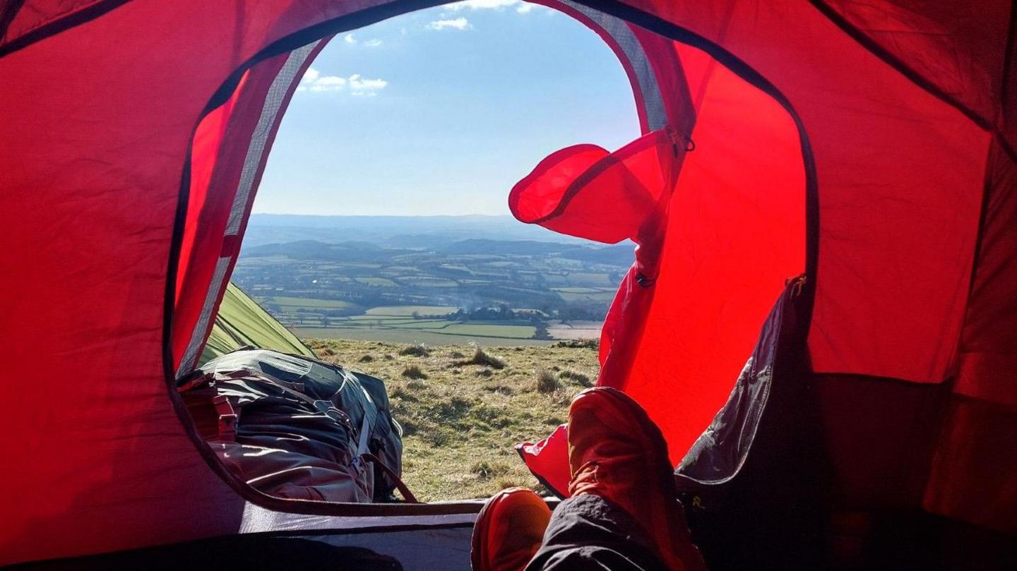 Marc Jeffrey sitting inside a red tent. The doorway to the tent is open and exposes stunning views across Dartmoor.