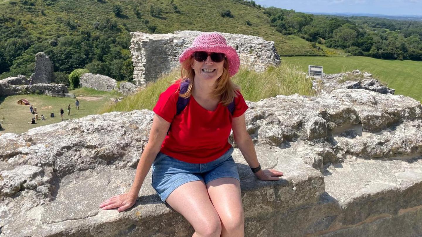 Kelly Burton is seen sat on a wall in the sunshine